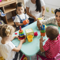 Children at nursery, sitting at table with teacher with stacking cups and other toys