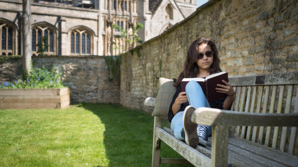 Exterior view of Burford School, showcasing historic architecture, well-maintained school grounds with a teenage girl on bench studying.