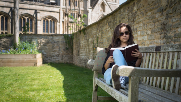 Exterior view of Burford School, showcasing historic architecture, well-maintained school grounds with a teenage girl on bench studying.