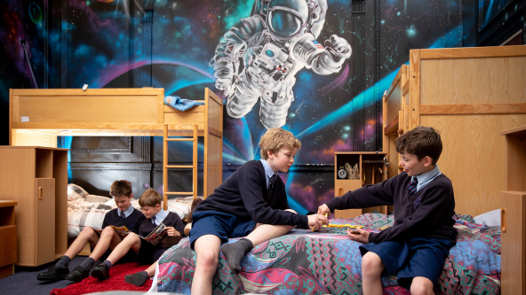 Boarder at Cheam School play games and read on beds in the dormitory