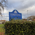 The sign of Chiswick School with the playing fields and main school building in the background