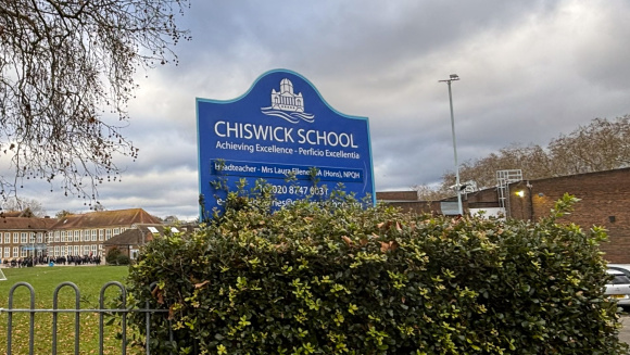The sign of Chiswick School with the playing fields and main school building in the background
