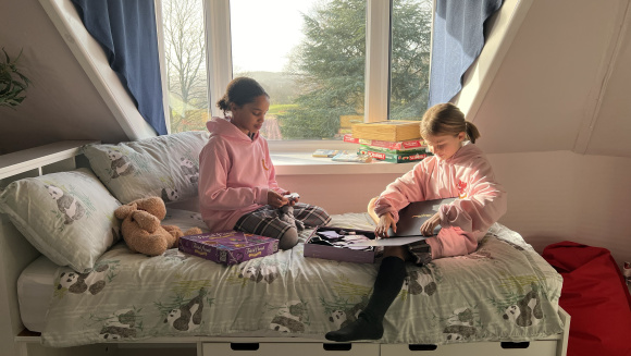 Two girl boarders at Hall Grove School sit on a bed in the boarding house