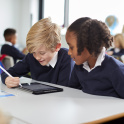 Two primary pupils - a girl and boy - sitting at a classroom table and working on a tablet