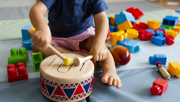 Nursery school child plays with drum surrounded by other toys
