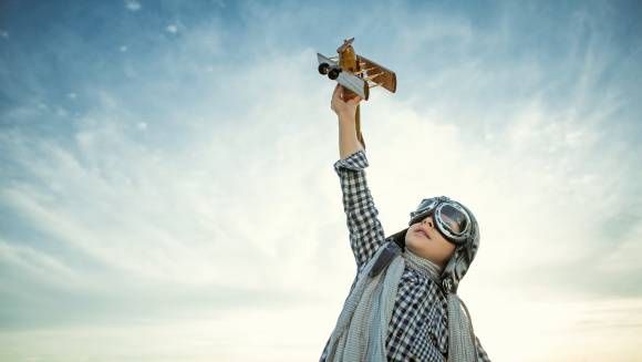 A child dressed as a pilot flying a toy aeroplane