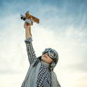 A child dressed as a pilot flying a toy aeroplane