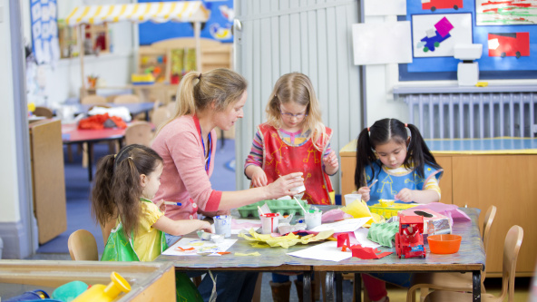 Children at nursery, sitting at table with teacher doing arts and crafts