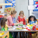 Children at nursery, sitting at table with teacher doing arts and crafts