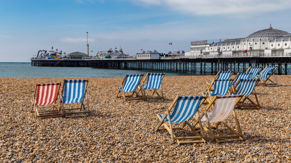 A view of Brighton Pier from the pebble beach with striped deckchairs in the foreground
