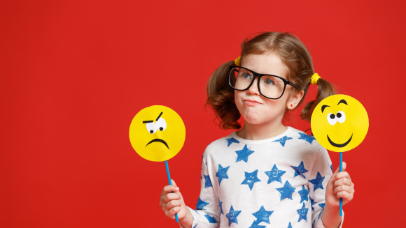 A child holding two paddles, one with a sad face and another with a happy face