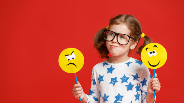 A child holding two paddles, one with a sad face and another with a happy face