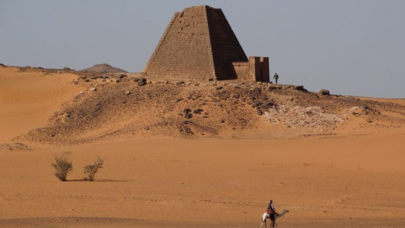 Khartoum desert with pyramid brick structure and person riding a camel