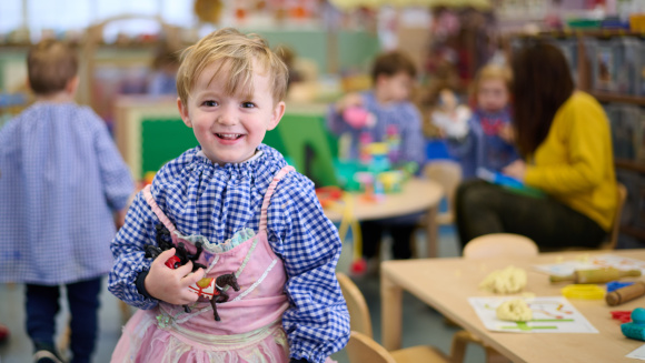 A child in art smock and princess dress at King&rsquo;s House nursery