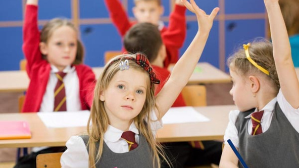 young girl in a prep classroom with a raised hand. Blurred children in the background with raised hands in red school uniform