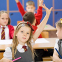 young girl in a prep classroom with a raised hand. Blurred children in the background with raised hands in red school uniform