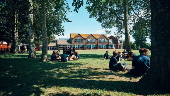 A sunny day at The Priory School with pupils sitting in the shade of the trees