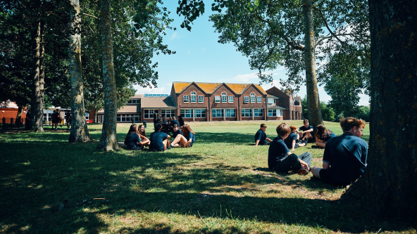 A sunny day at The Priory School with pupils sitting in the shade of the trees