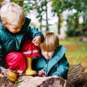 Two preschool-age children at St Andrew&rsquo;s Nursery sit on a fallen tree trunk