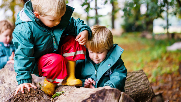 Two preschool-age children at St Andrew&rsquo;s Nursery sit on a fallen tree trunk