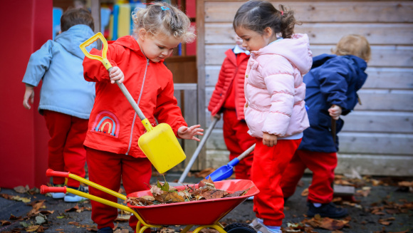 Two pre-school children at St Hilda's School gather fallen leaves in a children's wheelbarrow
