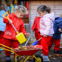 Two pre-school children at St Hilda's School gather fallen leaves in a children's wheelbarrow