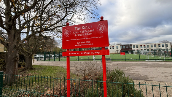 The school sign of The King&rsquo;s Church of England Primary School, with the school buildings and astroturf in the background