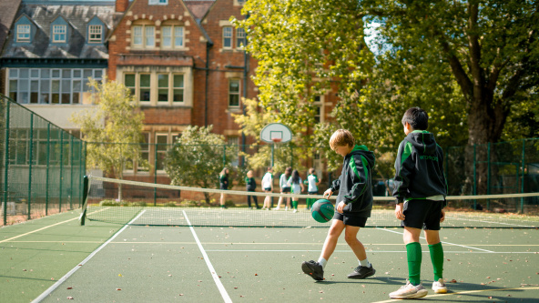 Two pupils play with a basketball on a tennis court at Wychwood School