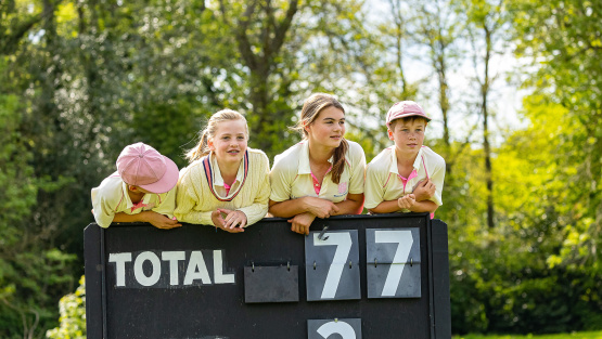 Elstree pupils in cricket whites lean on the back of a cricket score board