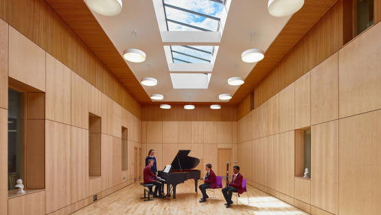 At Fettes College, a music rehearsal room, lined with birch ply and with striking skylights, pupils playing piano, guitar and bassoon