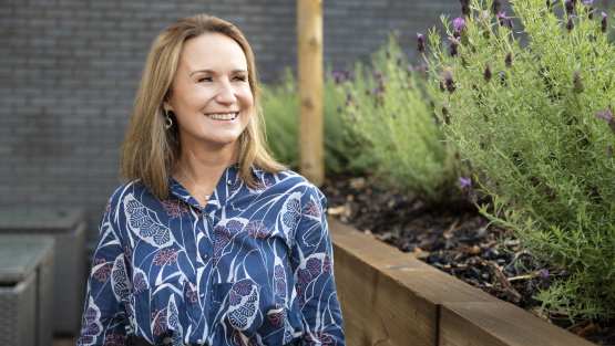 A portrait of Jo Beer, MD of Bursary Assessment Associates, taken outside next to a raised bed with lavender to her side..