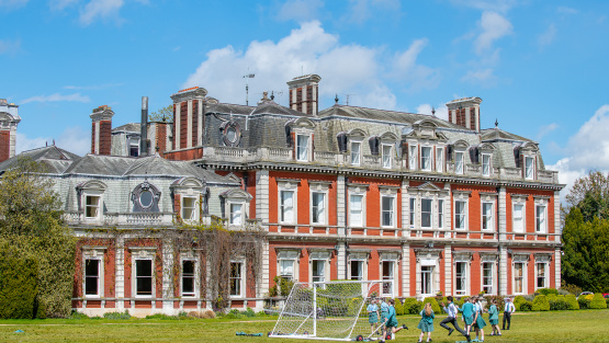 Exterior of independent school with school children playing football on a sports field