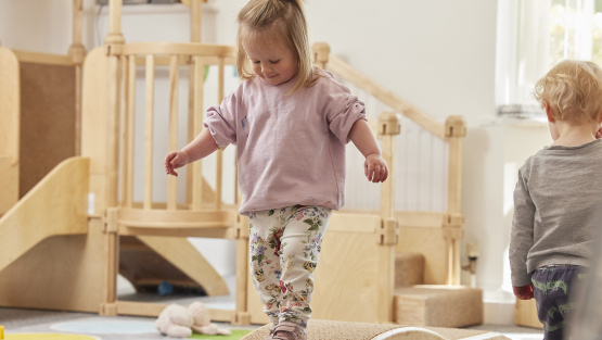 A toddler at Little Downend walks over wooden play apparatus