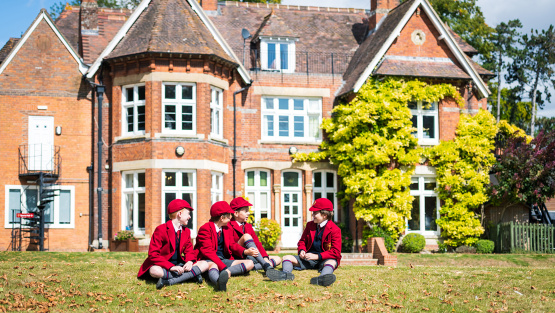 Pupils in red uniform sit on the grass outside at Moulsford School