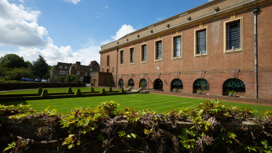 Exterior of independent school building and grounds that includes shrubbery, a path outlined with trimmed hedges