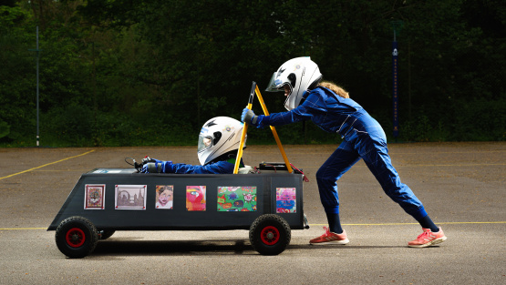 Two pupils in helmets and safety suits and with a soap box car