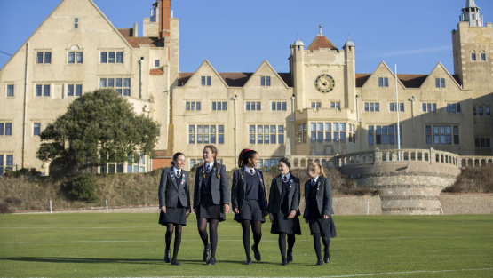 Five smiling pupils in uniform walk towards the camera with the imposing buildings of Roedean School as the backdrop