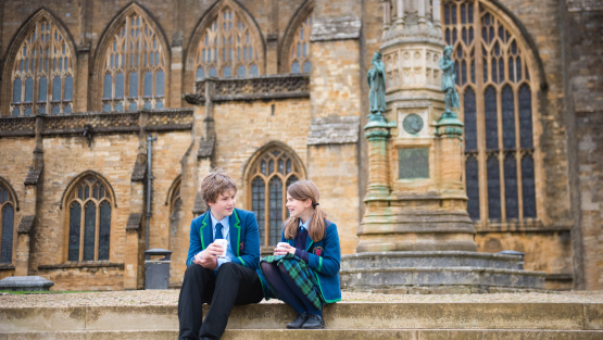 Exterior photo of Sherborne Prep with a young boy and girl sat on the steps smiling and talking in school uniform