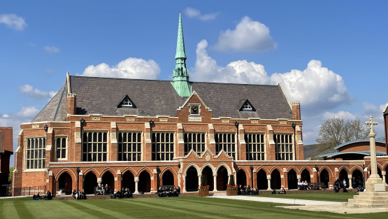 Pupils sitting outside the school hall of St John's Leatherhead on a sunny day.