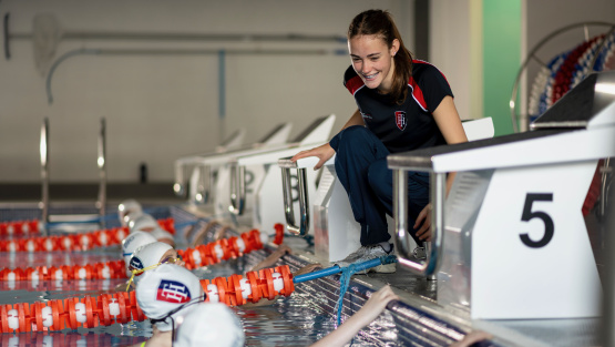 A girl at the side of the pool talks to the pupils in the water lining up to race