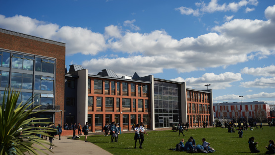 Main building of The Tiffin Girls' School, Kingston, with pupils sitting on the grass during breaktime