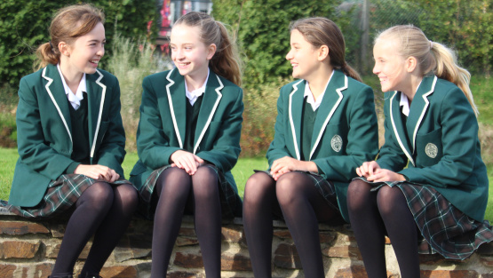 Truro High Year 7 students, in smart green uniform, sit on a wall and chat by the school lawns