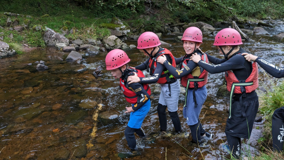 Pinewood year 5 pupils wearing helmets and life vests walking into a river at Dolygaer, south Wales